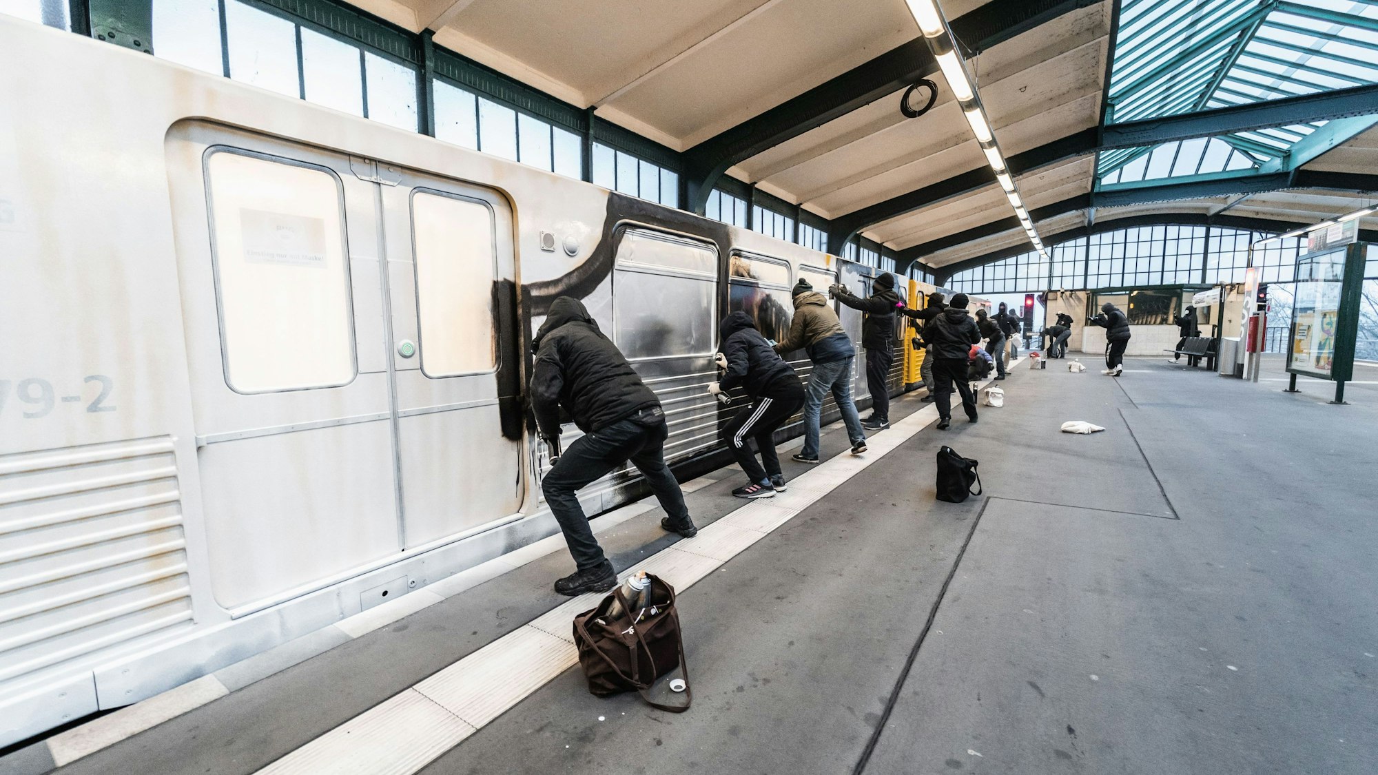 Mehrere vermummte Menschen sprühen Farbe auf einen U-Bahn-Waggon.