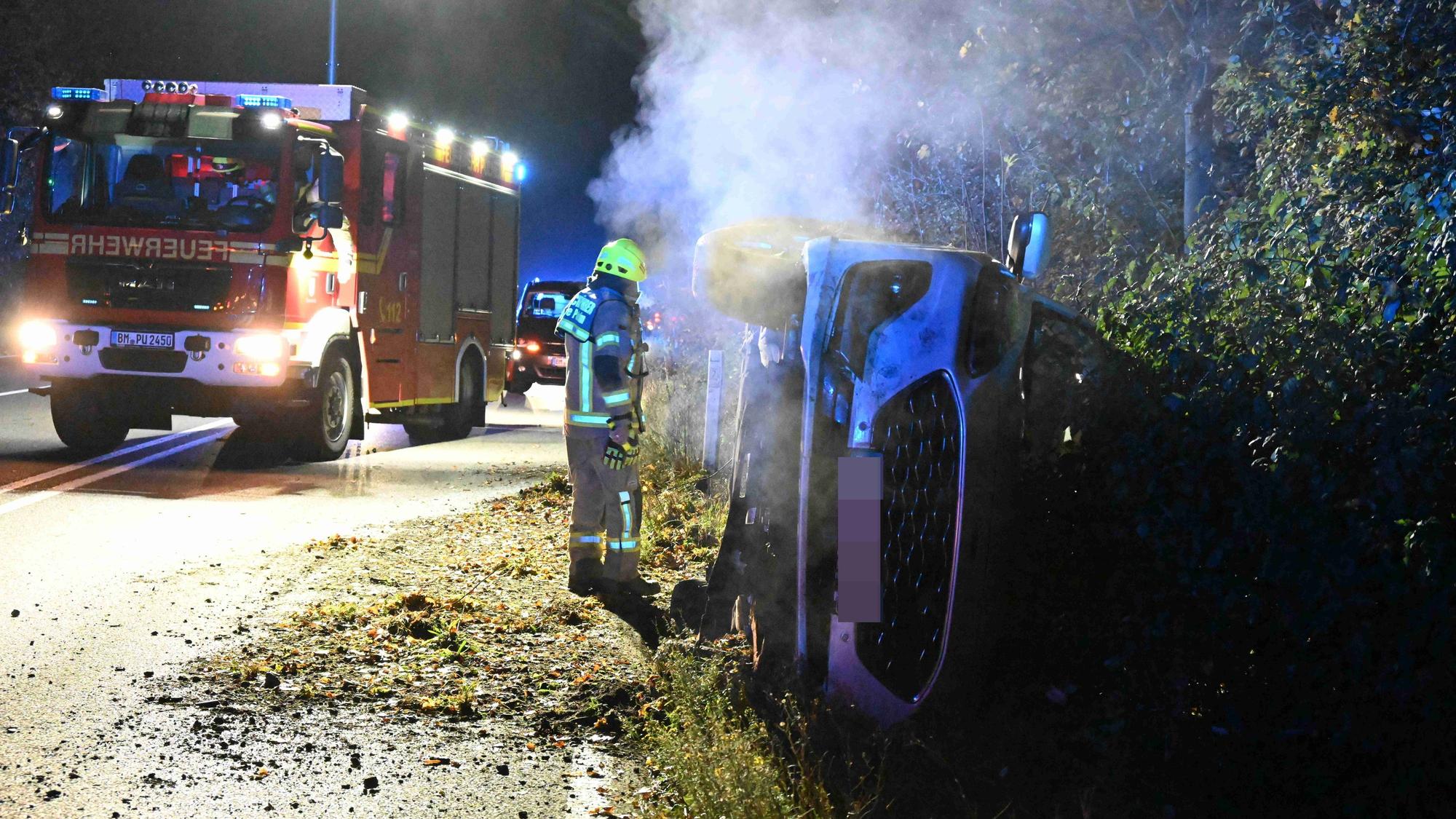 Das Unfallauto liegt umgekippt im Straßengraben. Im Hintergrund steht ein Feuerwehrauto.