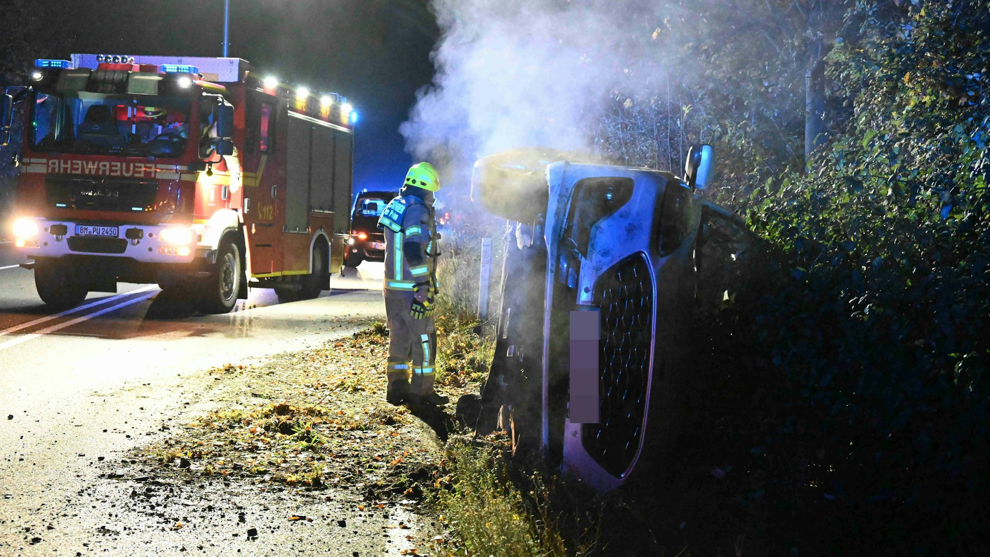 Das Unfallauto liegt umgekippt im Straßengraben. Im Hintergrund steht ein Feuerwehrauto.