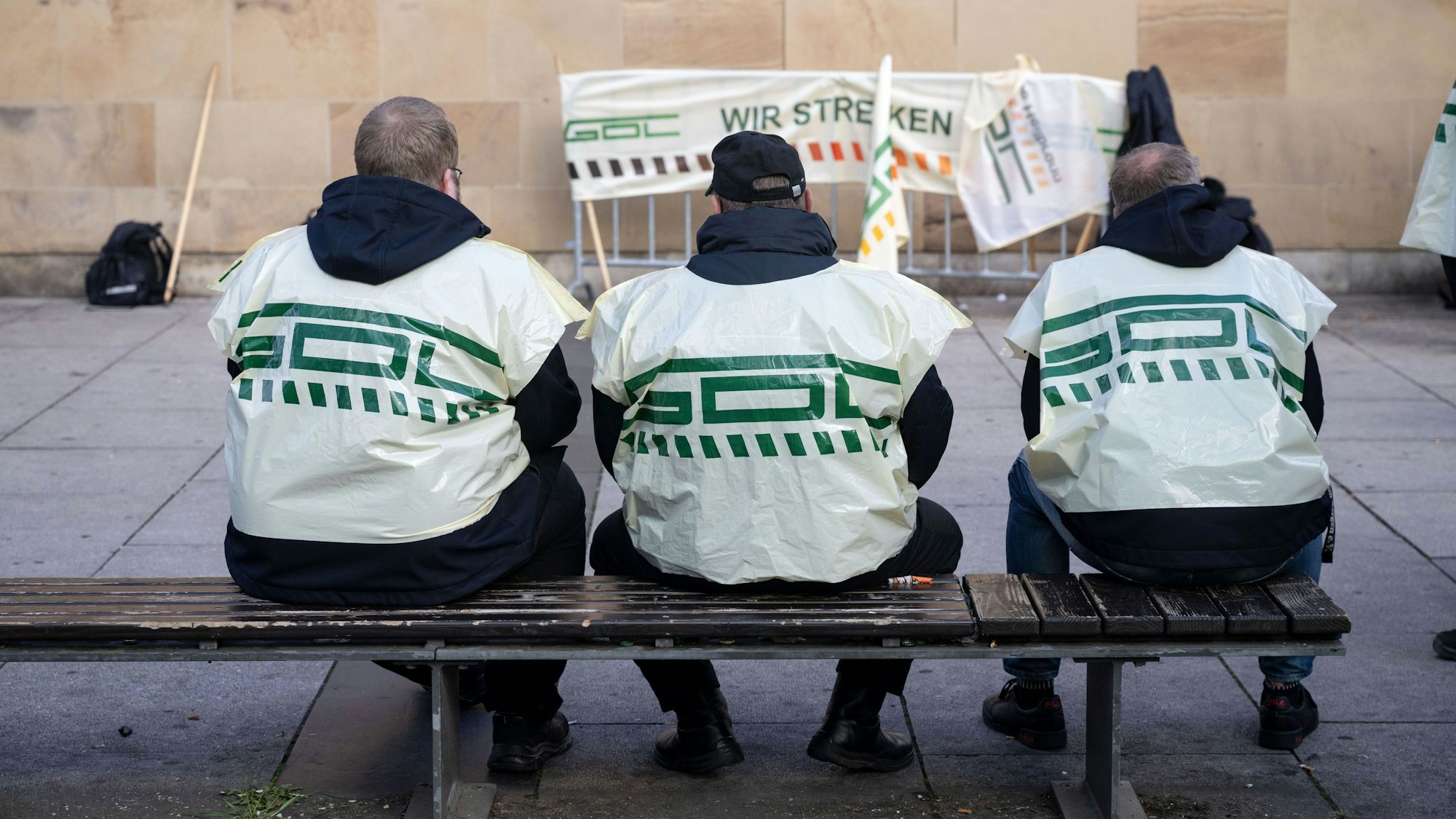 Teilnehmer eines Warnstreiks der Gewerkschaft Deutscher Lokomotivführer (GDL) sitzen vor einem Hauptbahnhof auf einer Bank. Die Gewerkschaft hat neue Streiks beschlossen.