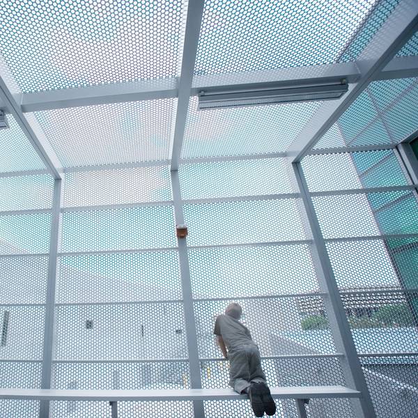 Ein Junge kniet auf einer Bank und schaut durch Gitter ins Freie.