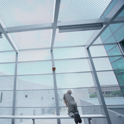 Ein Junge kniet auf einer Bank und schaut durch Gitter ins Freie.