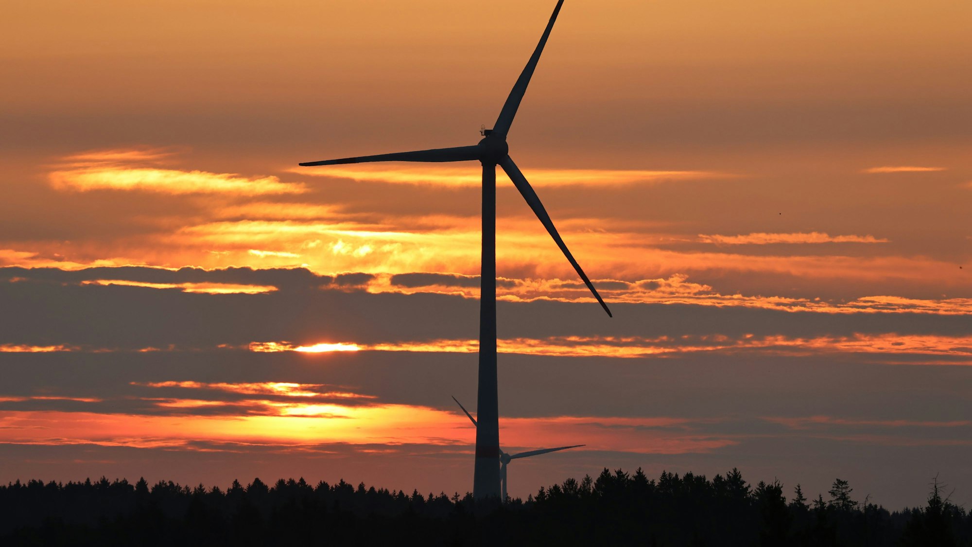 Eine Windkraftanlage auf einer Wiese vor der untergehenden Sonne.