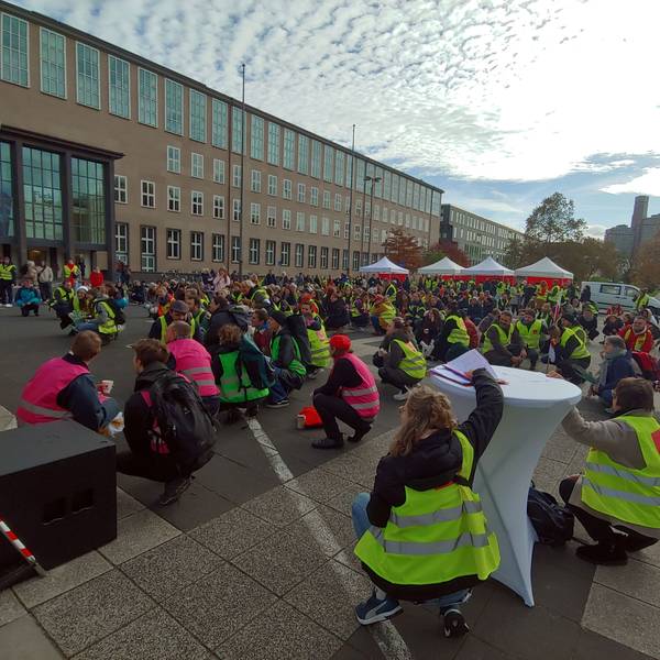 Teilnehmer und Teilnehmerinnen des Warnstreiks sitzen auf dem Boden