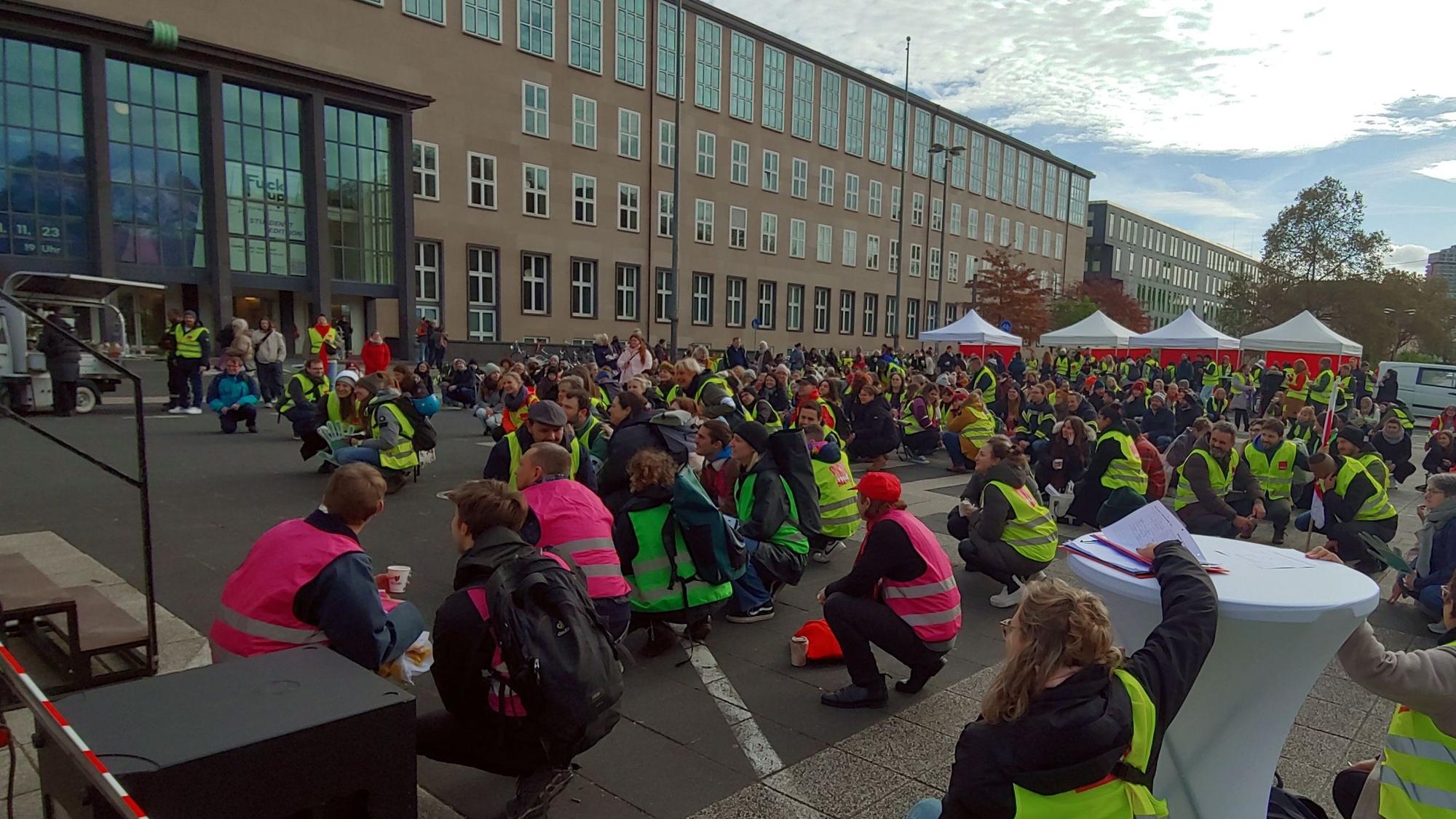 Teilnehmer und Teilnehmerinnen des Warnstreiks sitzen auf dem Boden