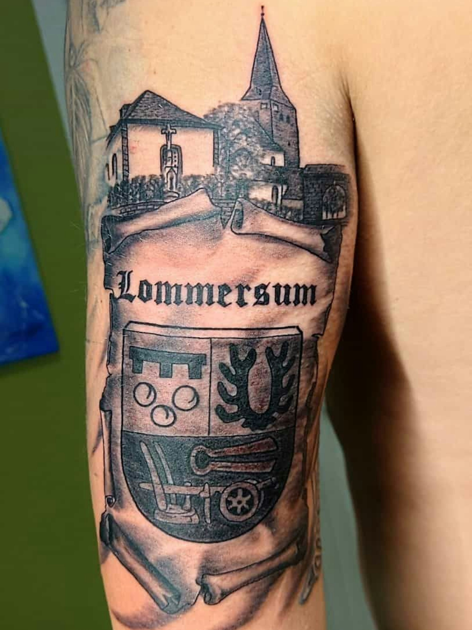 Das Bild zeigt das Tattoo von Dominik Schöpfer. Es ist die Lommersumer Kirche und das Dorfwappen zu erkennen.