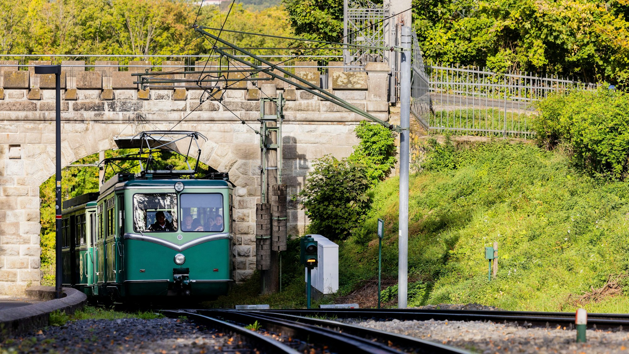 Die Drachenfelsbahn fährt auf Schienen hoch zum Drachenfels an noch grünen Bäumen entlang.