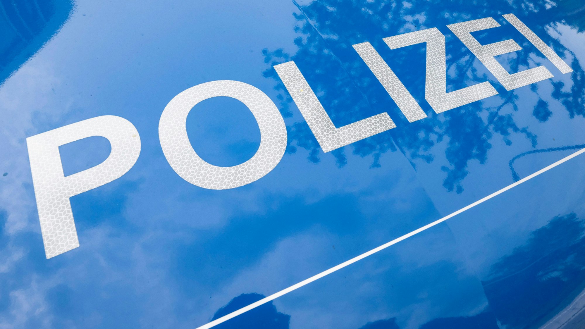 Das Foto zeigt die Motorhaube eines Polizeiwagen, darauf ist in großen weißen Buchstaben auf blauem Grund das Wort „Polizei “zu lesen.