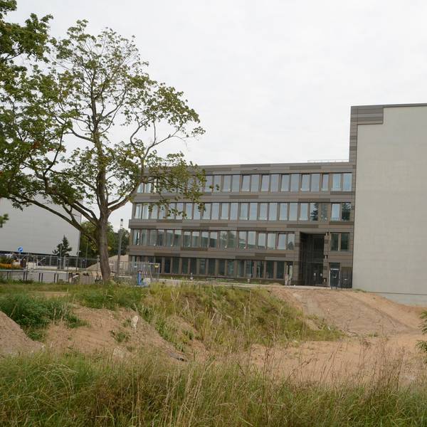Ein modernes Bürogebäude mit vier Etagen; am Querbau markiert eine graue Fläche den geplanten Hotel-Anbau.