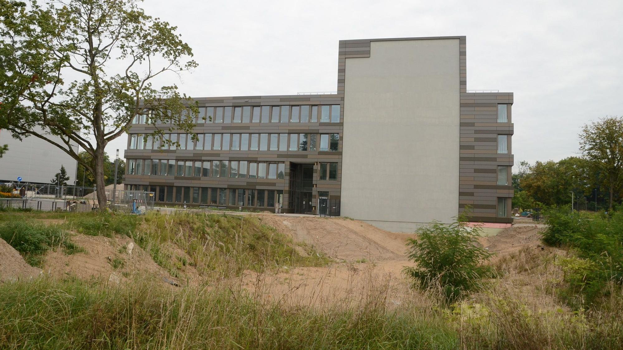 Ein modernes Bürogebäude mit vier Etagen; am Querbau markiert eine graue Fläche den geplanten Hotel-Anbau.