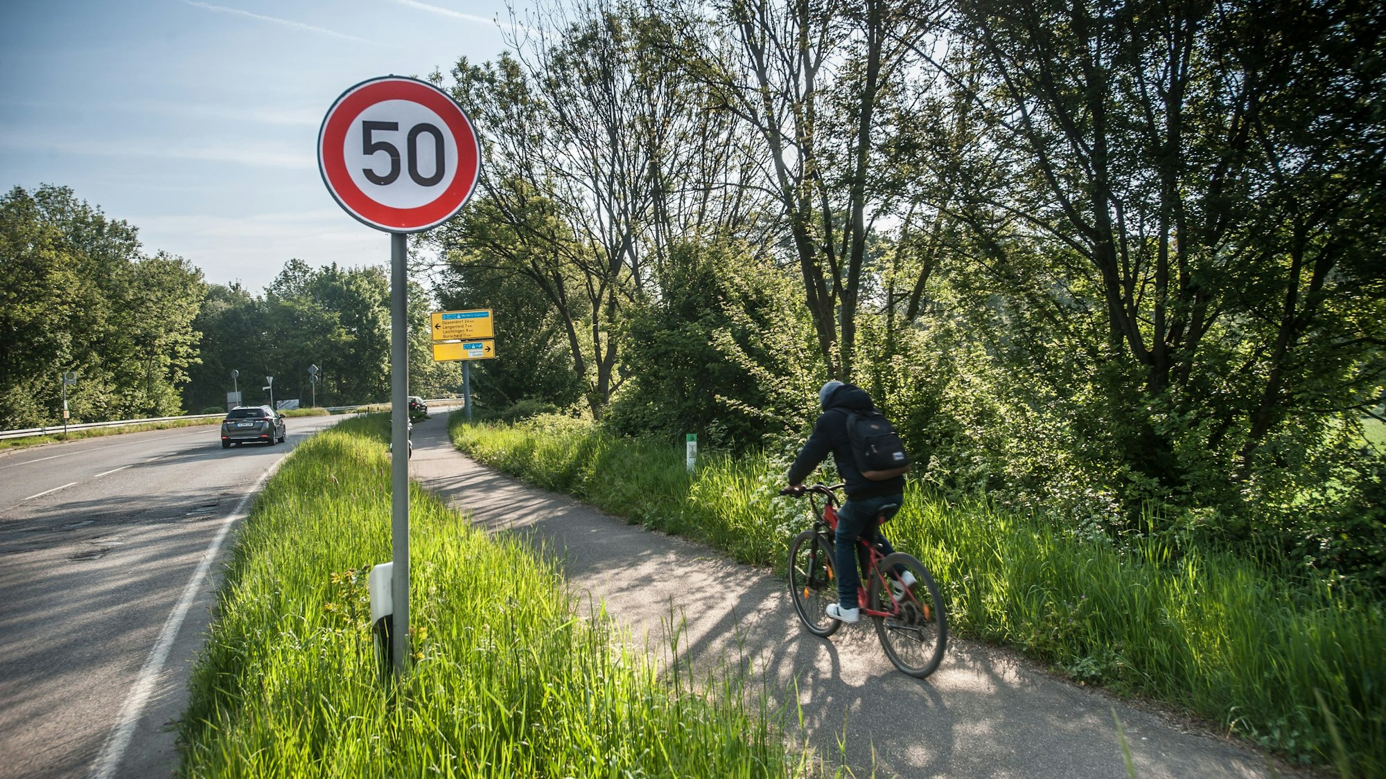 Ein Radfahrer fährt auf einem Radwege neben einer Grünfläche.