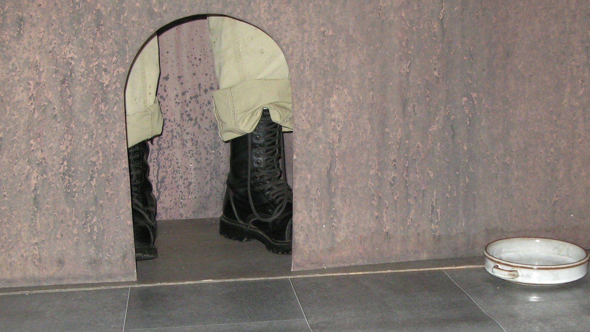 Das Bild aus dem Innern einer begehbaren Skulptur empfindet das Innere der Hundehütte nach, in der sich Tamar Dreifuss als Kind mit ihrer Mutter versteckt hat. Hinter der Öffnung steht ein Paar Soldatenstiefel.