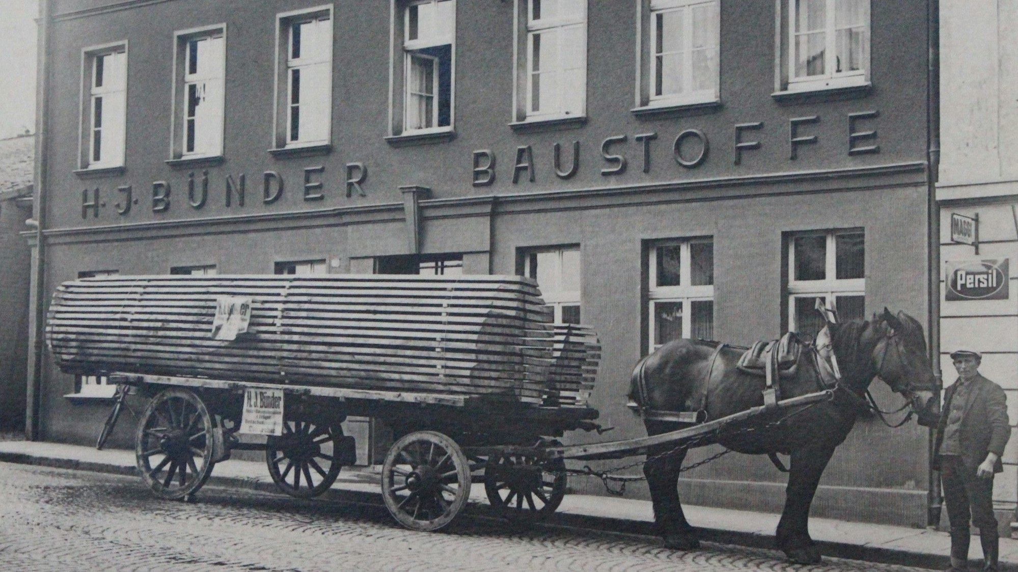 Das historische Foto zeigt ein Firmengebäude von Bünder in Euskirchen. Davor steht ein Wagen voller Bretter, der von einem Pferd gezogen wird.