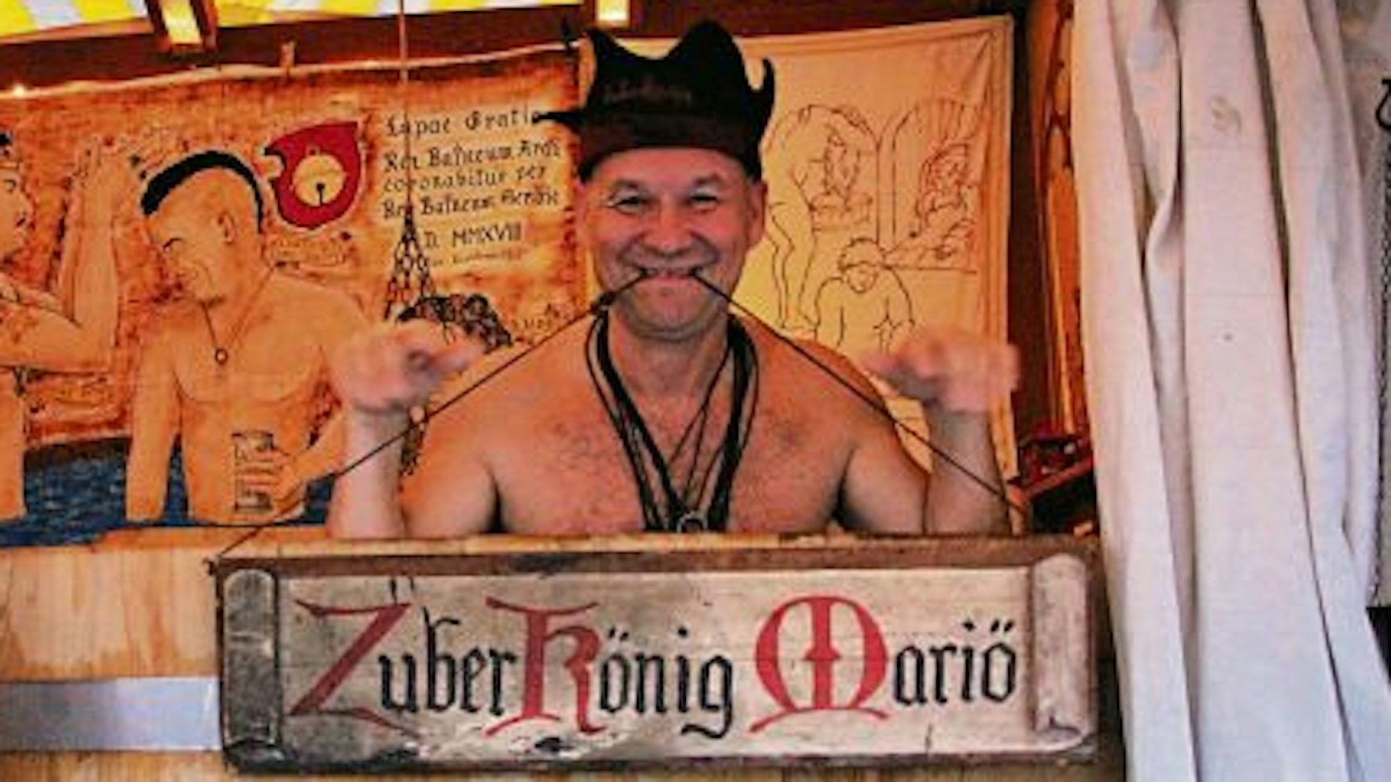 Mit freiem Oberkörper hockt der Zuberkönig Mariö in einem Badezuber aus Holz.