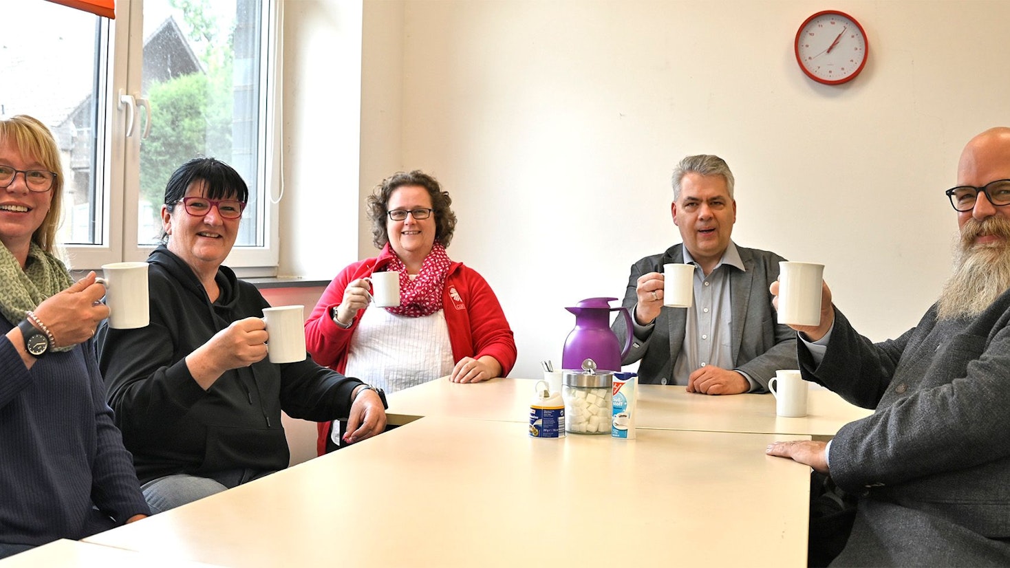 Drei Frauen und zwei Männer sitzen an einem Tisch und halten Tassen in den Händen.