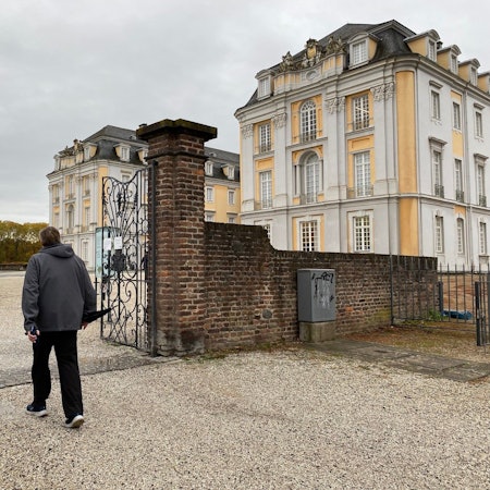 Zu sehen ist ein Spaziergänger, der den Park vor Schloss Augustusburg betritt.