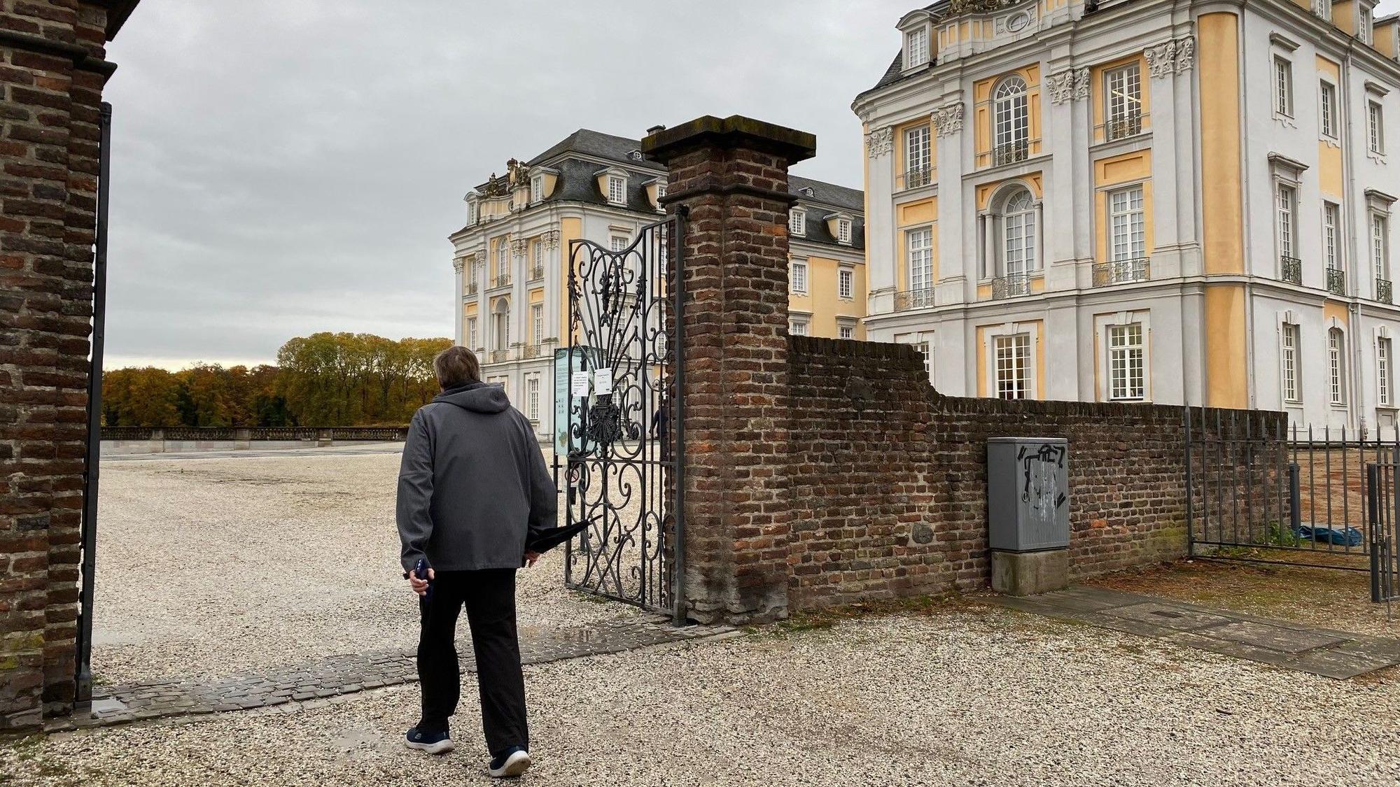 Zu sehen ist ein Spaziergänger, der den Park vor Schloss Augustusburg betritt.