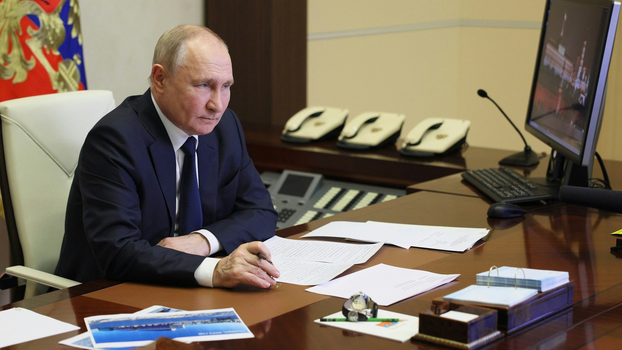 Der russische Präsident Wladimir Putin sitzt einem Schreibtisch, auf dem verschiedene Dokumente liegen und schaut auf einen Computerbildschirm.