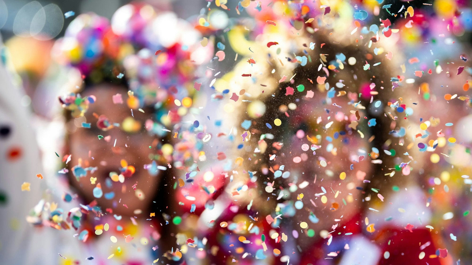 Konfetti fliegt vor bunt kostümierten Menschen durch die Luft.