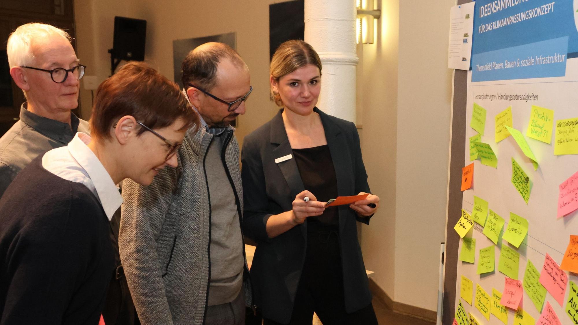 Maren Bogon (rechts) steht mit Teilnehmern des Bürgerworkshops in Engelskirchen vor einer Magnettafel mit vielen farblichen Post-It-Zetteln.