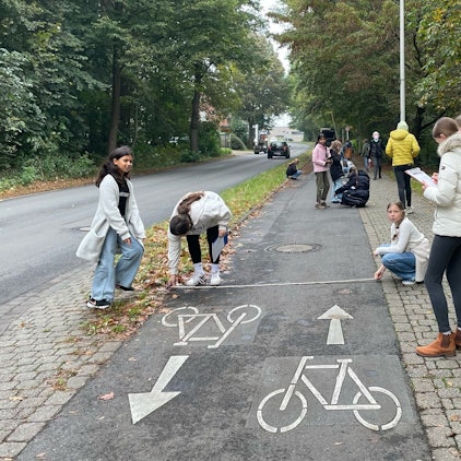 Auf dem Bild sind Schüler zu sehen, die eine Straße überprüfen