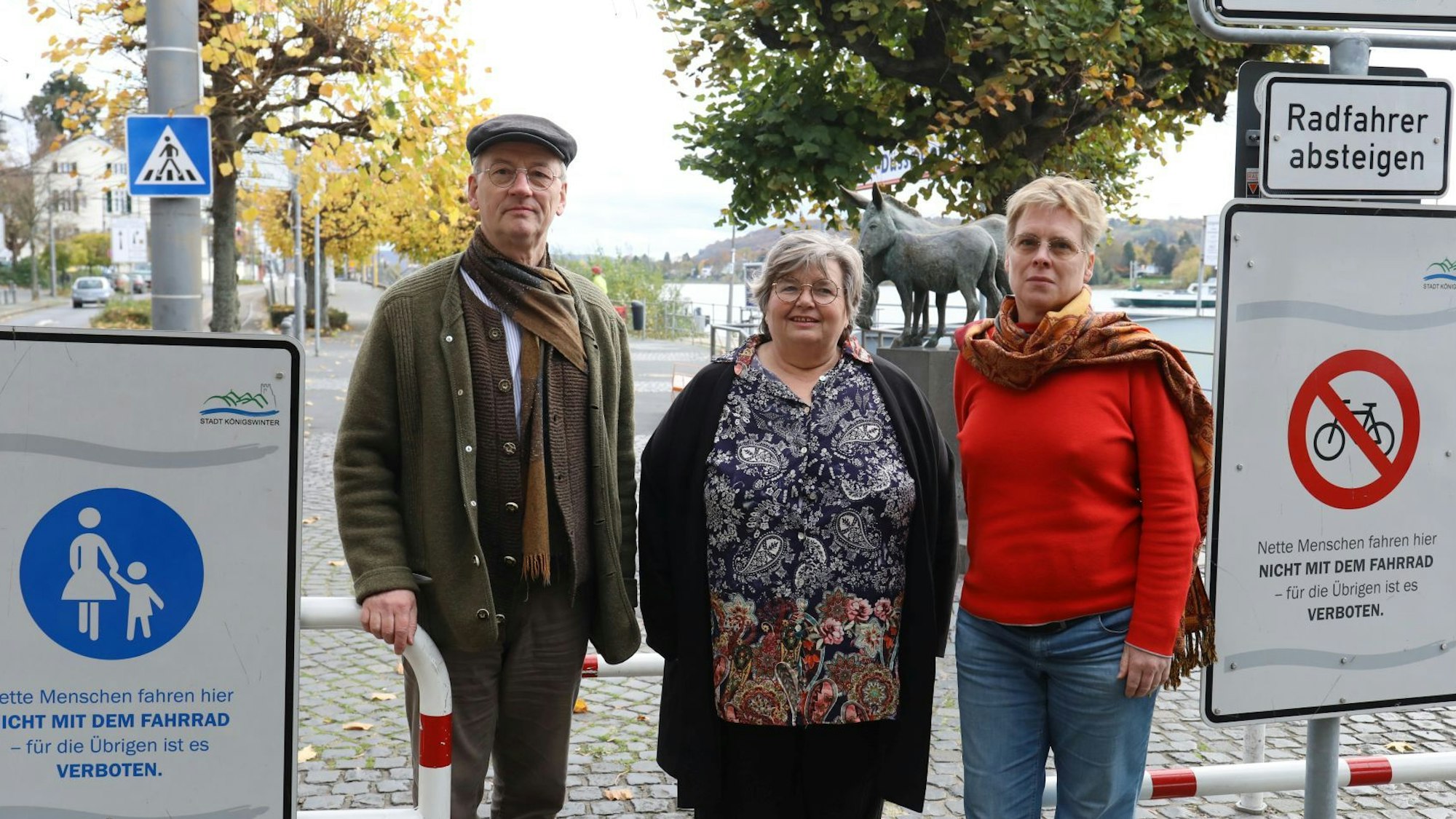 Drei Personen stehen auf der Rheinpromenade in Königswinter neben den Schildern, die das Radfahren in Höhe des Eselsbrunnens untersagen..