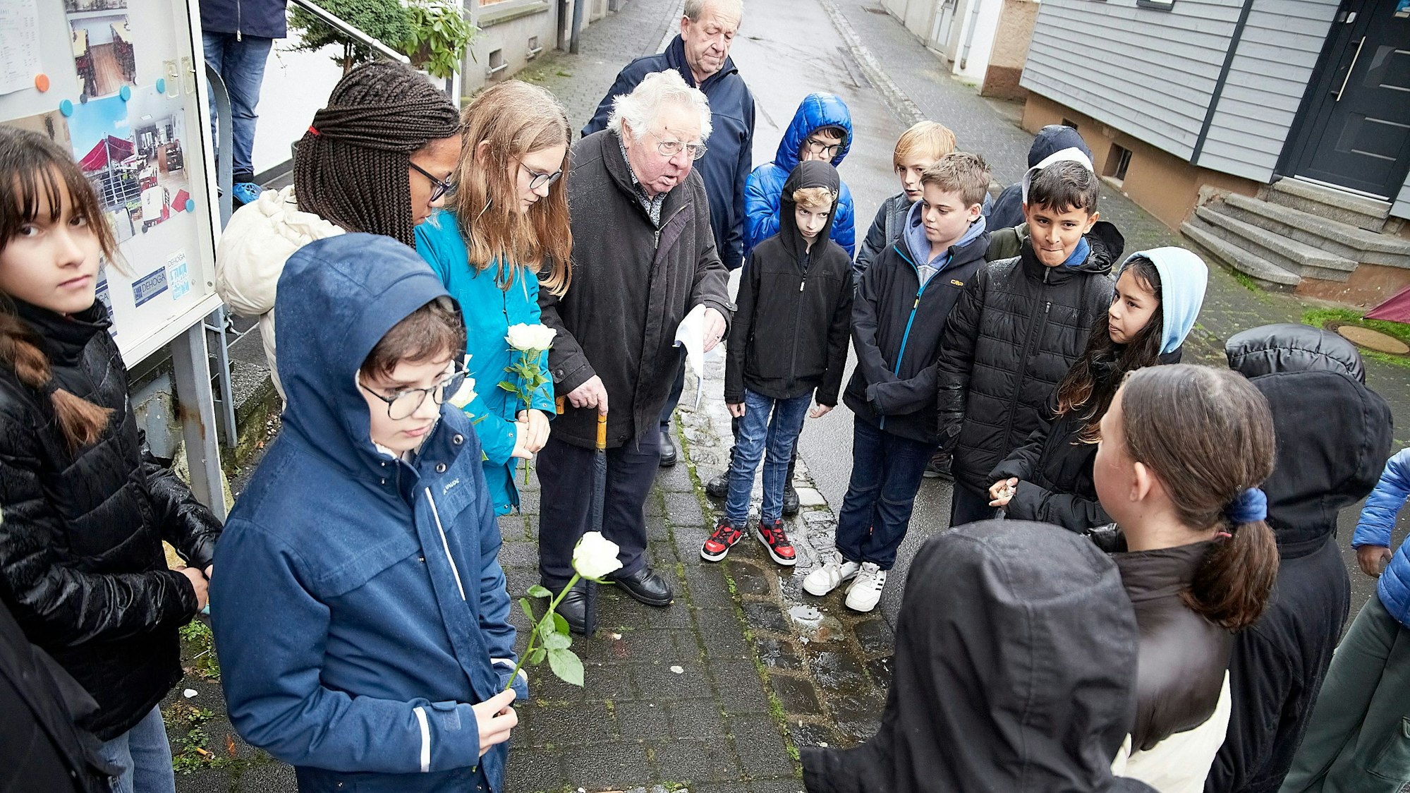 Alois Sommer mit einer Gruppe von Schulkindern. Einige tragen eine weiße Rose in der Hand.