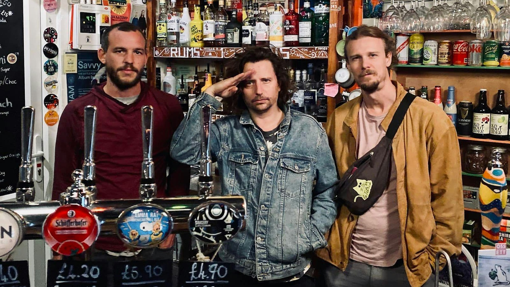 Drei Musiker stehen an der Zapfanlage eines englischen Pubs.