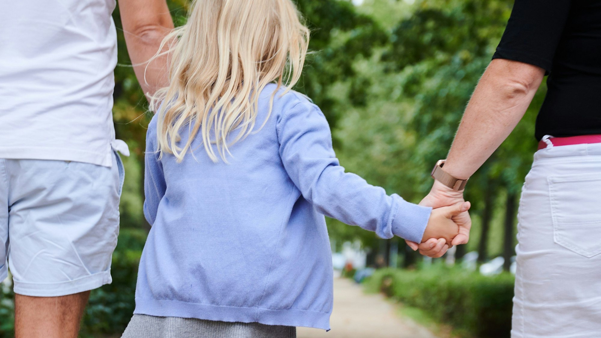 Ein Vater und eine Mutter halten die Hände ihrer Tochter, während sie auf einem Gehweg gehen. (Illustration)