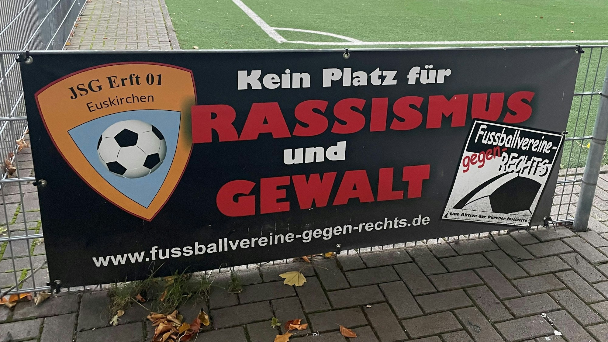Das Bild zeigt ein Schild mit der Aufschrift „Kein Platz für Rassismus und Gewalt“ auf dem Sportplatz der JSG Erft in Kuchenheim.