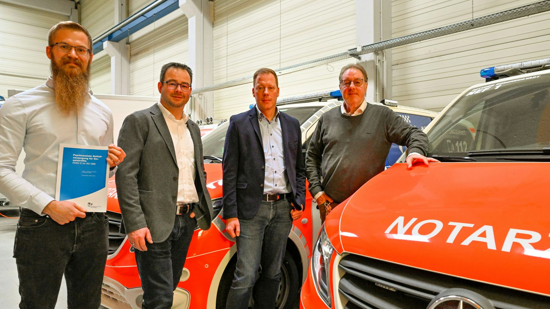 Die vier Männer stehen in einer Fahrzeughalle neben einem Notarztwagen.