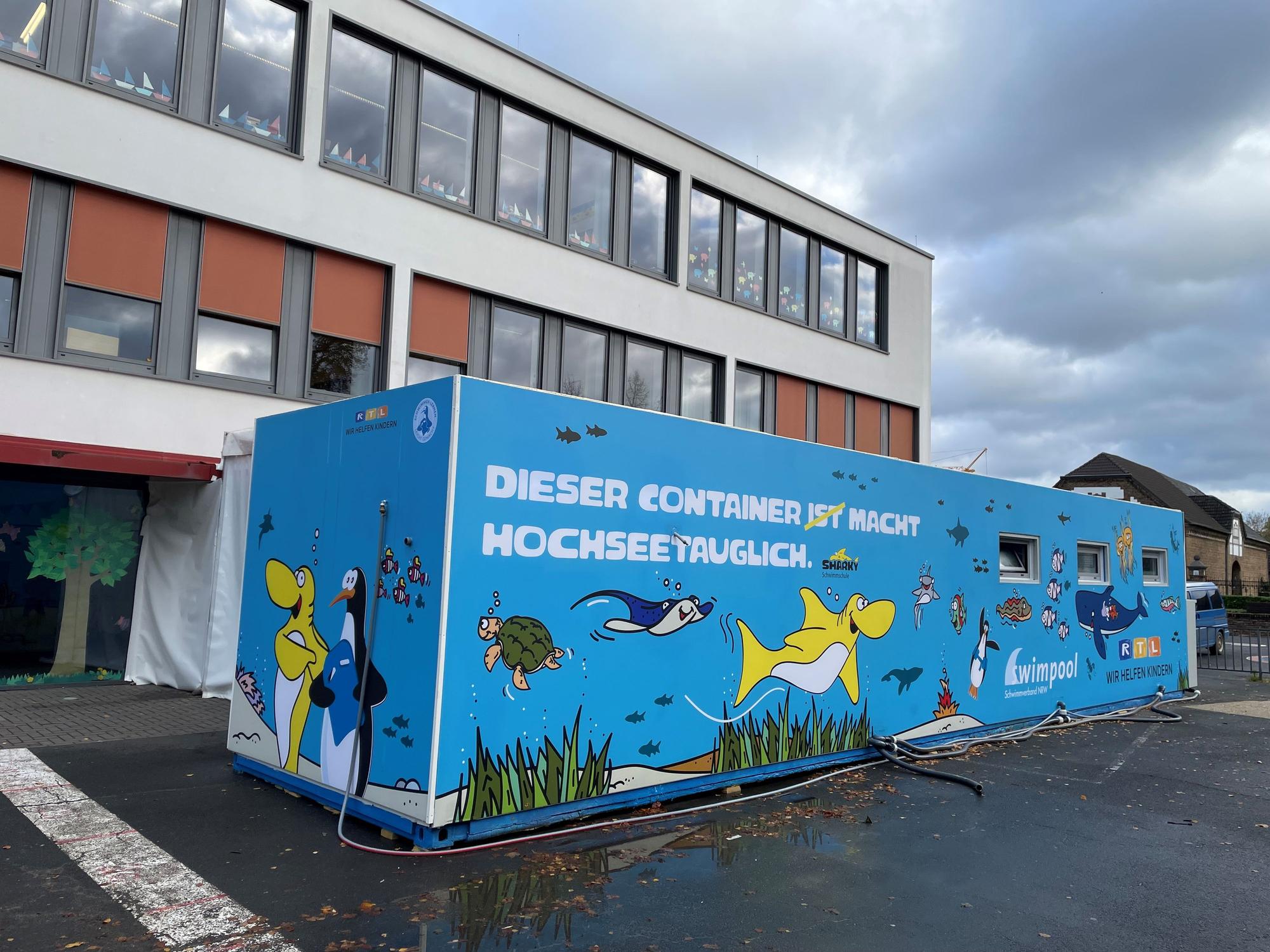 Ein als mobiles Schwimmbecken umgebauter Hochseecontainer steht auf einem Schulhof.