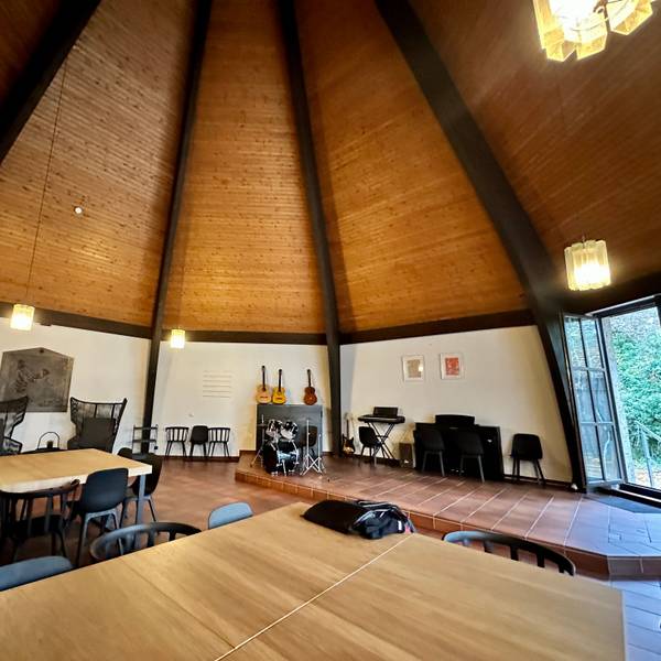 Der luftige Innenraum einer Kirche mit einer hohen holzverkleideten Decke bietet Platz für Tische, Stühle, Gitarren.