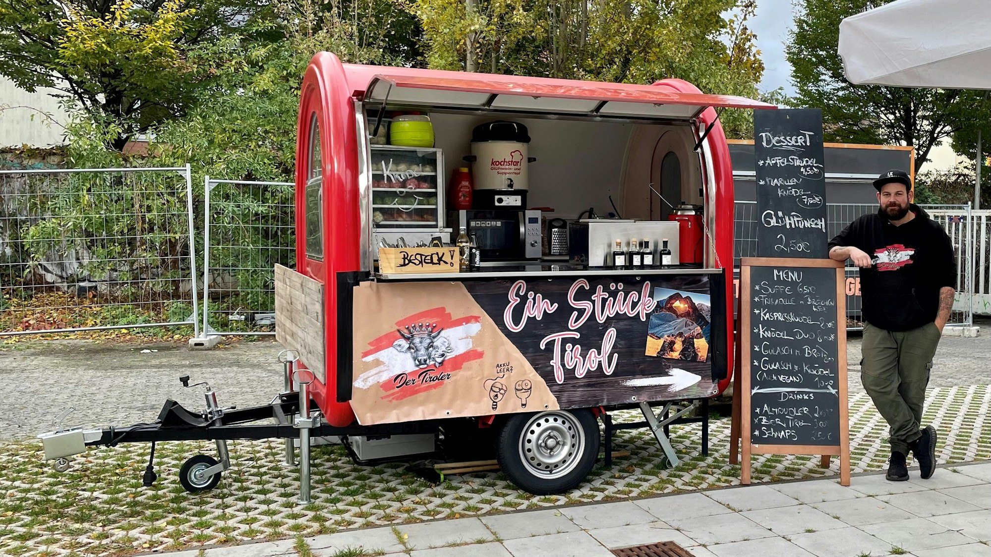 Marcel Kleewein steht neben einem roten Verkaufswagen, in dem er österreichische Spezialitäten verkauft.