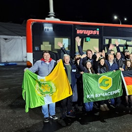 Menschen mit Fahnen stehen am Abend vor einem Linienbus.