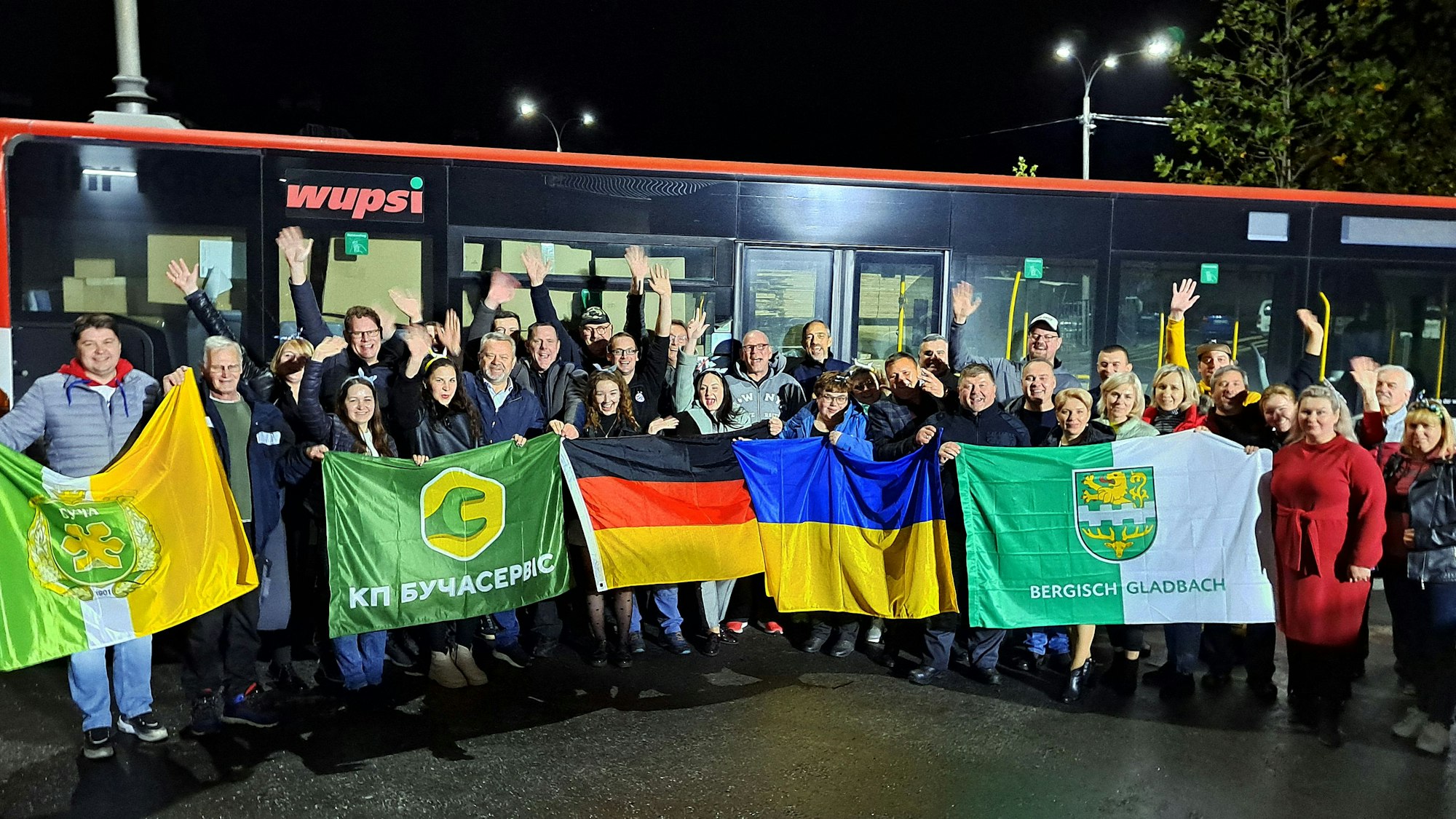 Menschen mit Fahnen stehen vor einem Bus in Butscha.