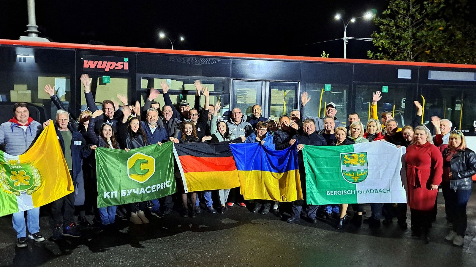 Menschen mit Fahnen stehen am Abend vor einem Linienbus.