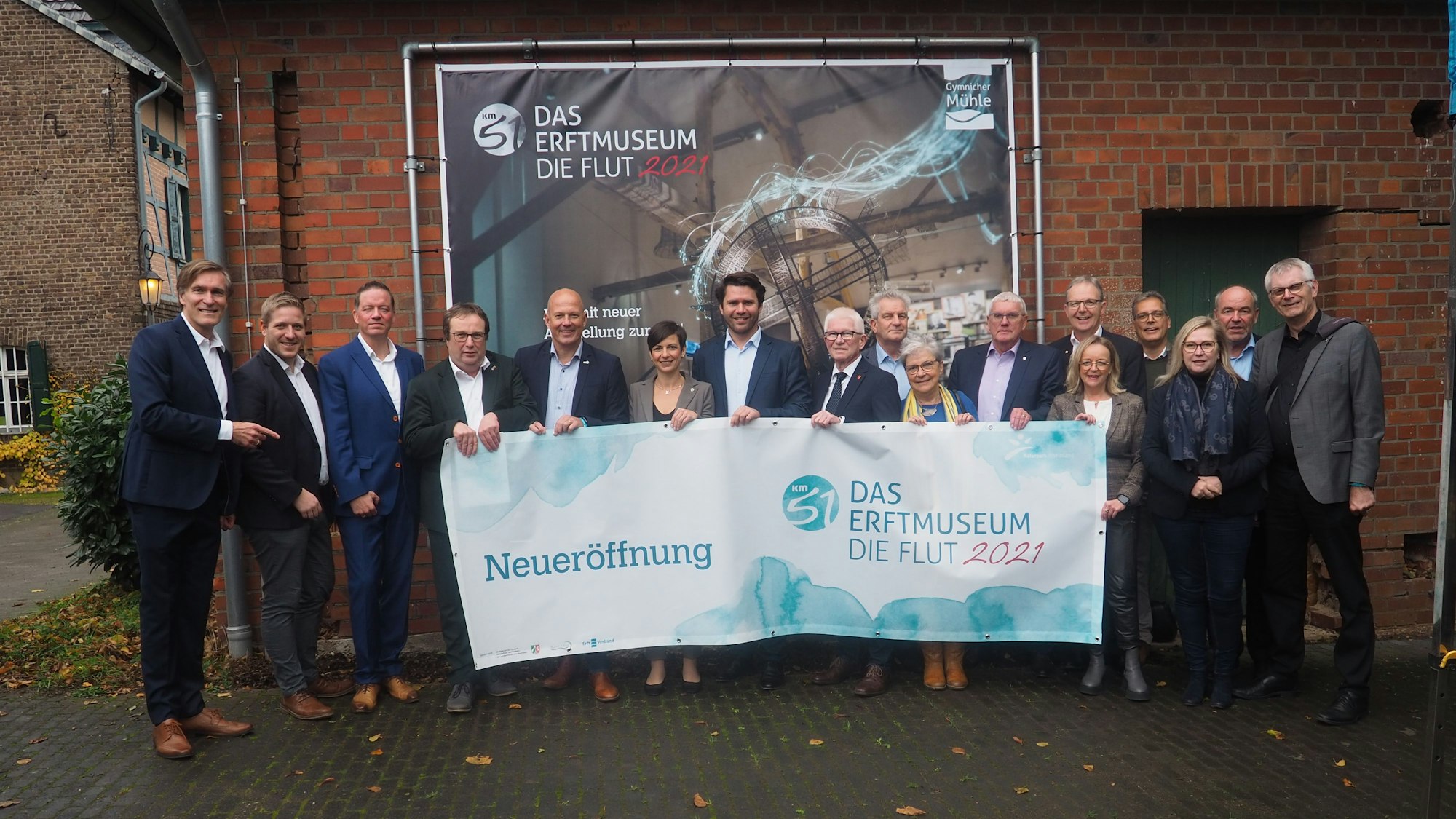 Eine Gruppe steht vor einem Plakat und hält ein Transparent, das auf die Eröffnung der Ausstellung hinweist.