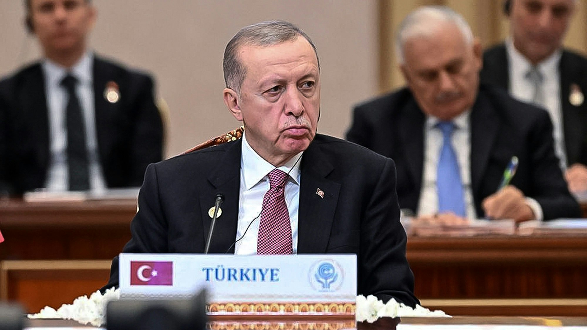 Recep Tayyip Erdogan, Präsident der Türkei, sitzt im Vordergrund an einem Pult mit der Aufschrift „Türkiye“, im Hintergrund sind andere Staats- und Regierungschefs zu sehen.