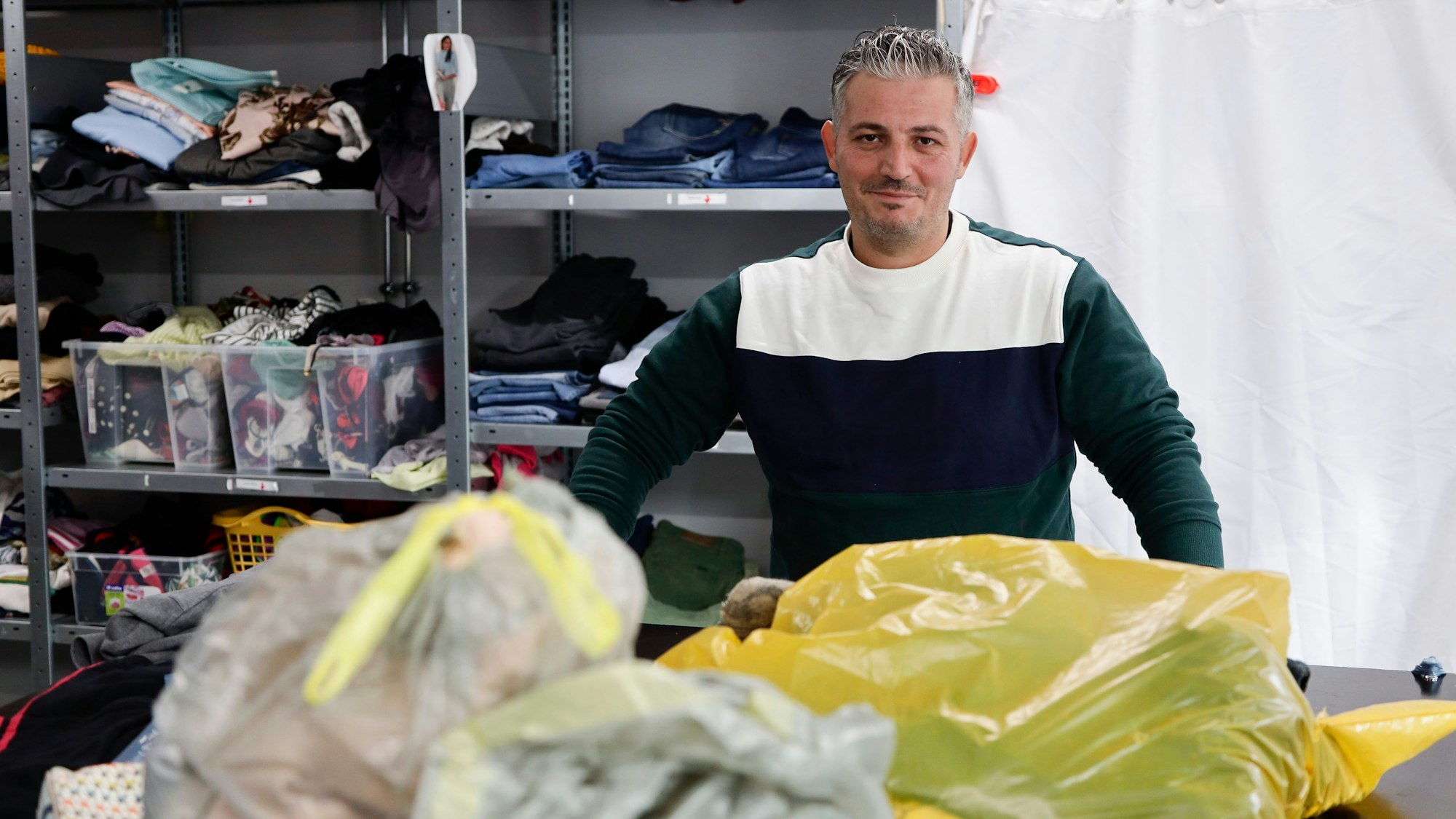 Mitarbeiter Ibrahim Bulut vom Deutschen Roten Kreuz steht vor gespendeten Kleidersäcken, die er gleich sortieren wird.