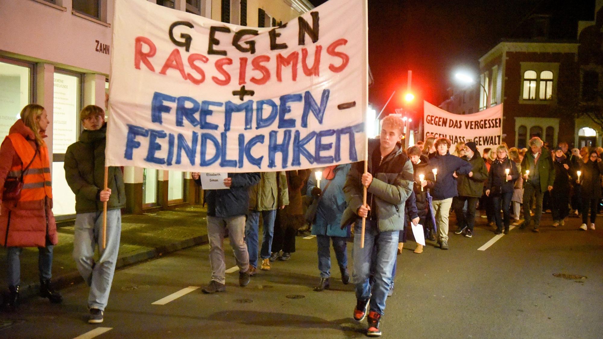 Auf dem Foto sind Teilnehmende des Schweigegangs zu sehen. Sie tragen Transparente. Auf einem ist zu lesen „Gegen Rassismus und Fremdenfeindlichkeit“.