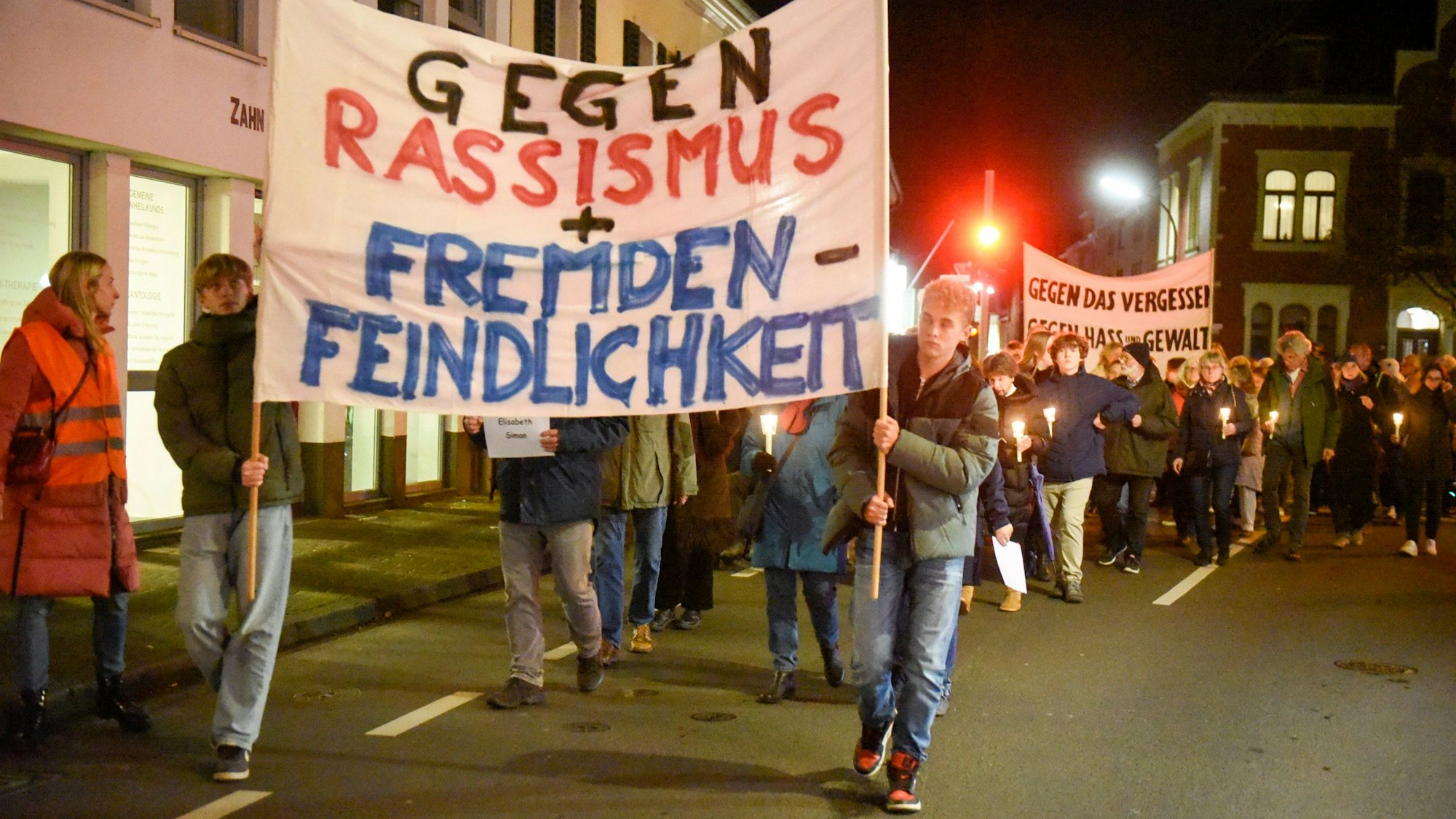 Auf dem Foto sind Teilnehmende des Schweigegangs zu sehen. Sie tragen Transparente. Auf einem ist zu lesen „Gegen Rassismus und Fremdenfeindlichkeit“.