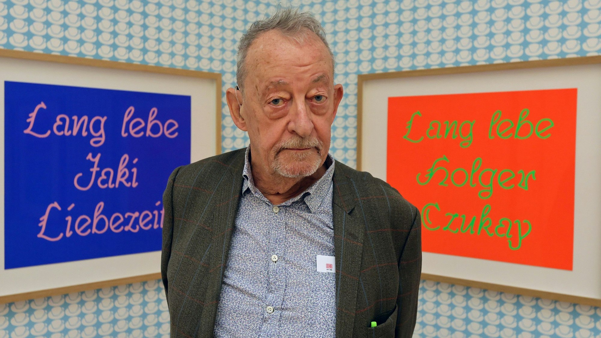 Kasper König steht vor zwei Kunstwerken und schaut in die Kamera.