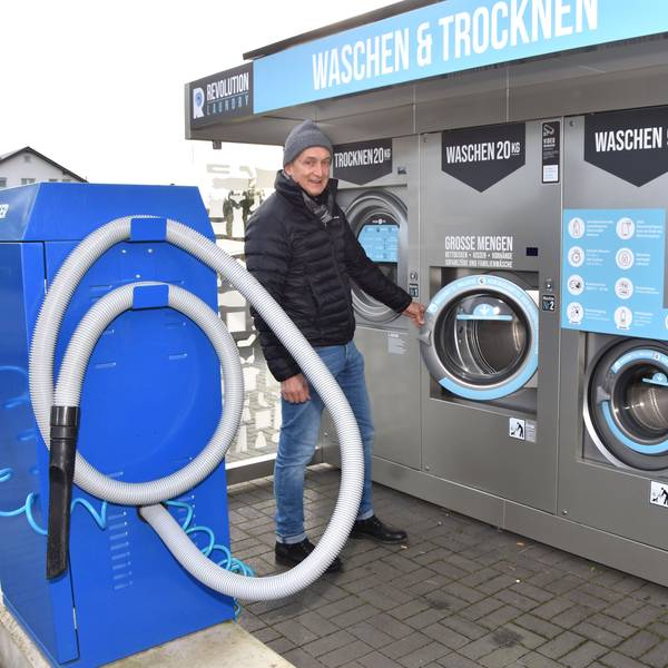 Ein Mann mit Mütze steht zwischen einem großen Autostaubsauger und großen Waschautomaten.