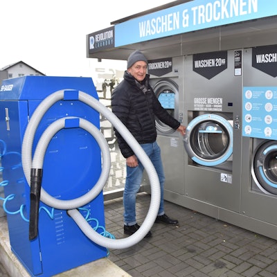 Ein Mann mit Mütze steht zwischen einem großen Autostaubsauger und großen Waschautomaten.