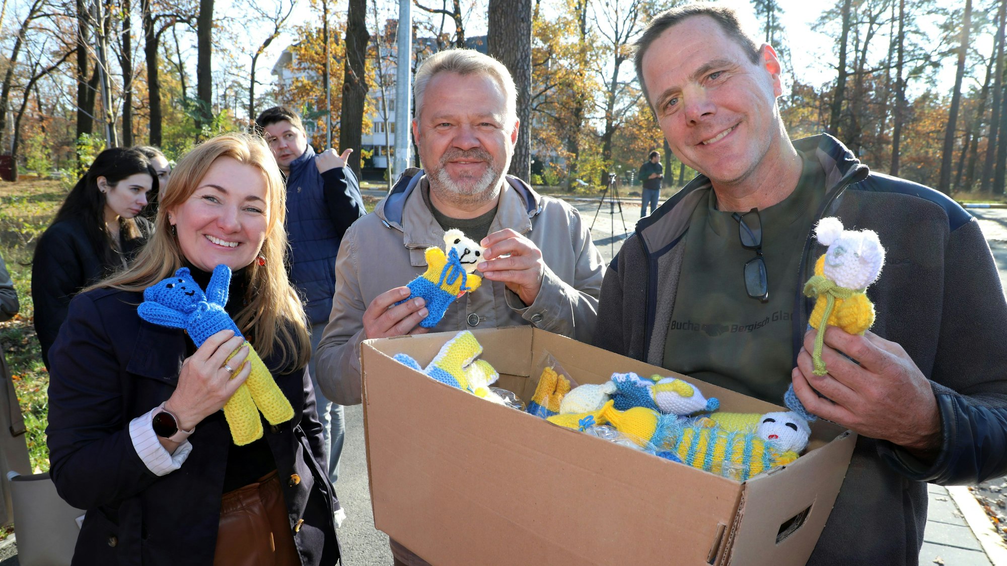 Drei Menschen halten einen Karton mit Stricktieren in den Händen.