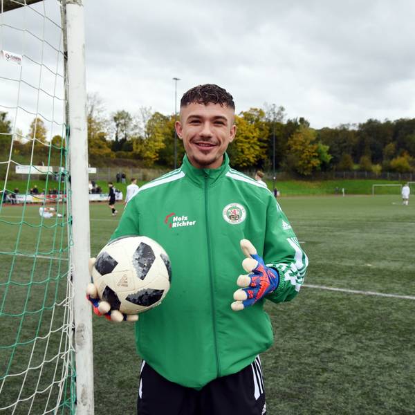 Ein Fußballspieler steht mit Torwarthandschuhen und Ball an einem Tor.