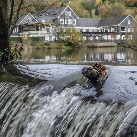 Von einem Stausee mit einem großem Haus im Hintergrund geht ein Bach ab.