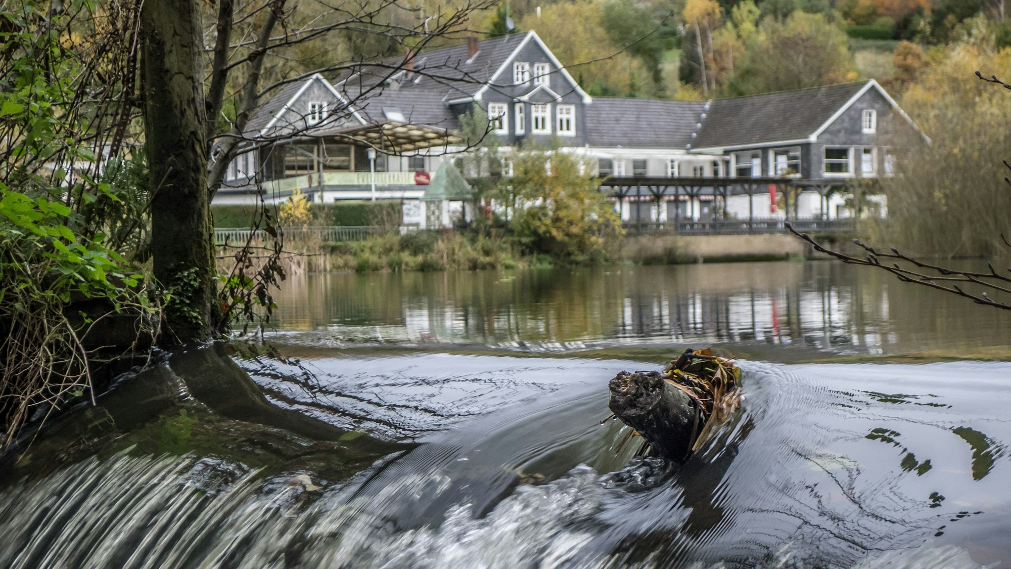 Von einem Stausee mit einem großem Haus im Hintergrund geht ein Bach ab.