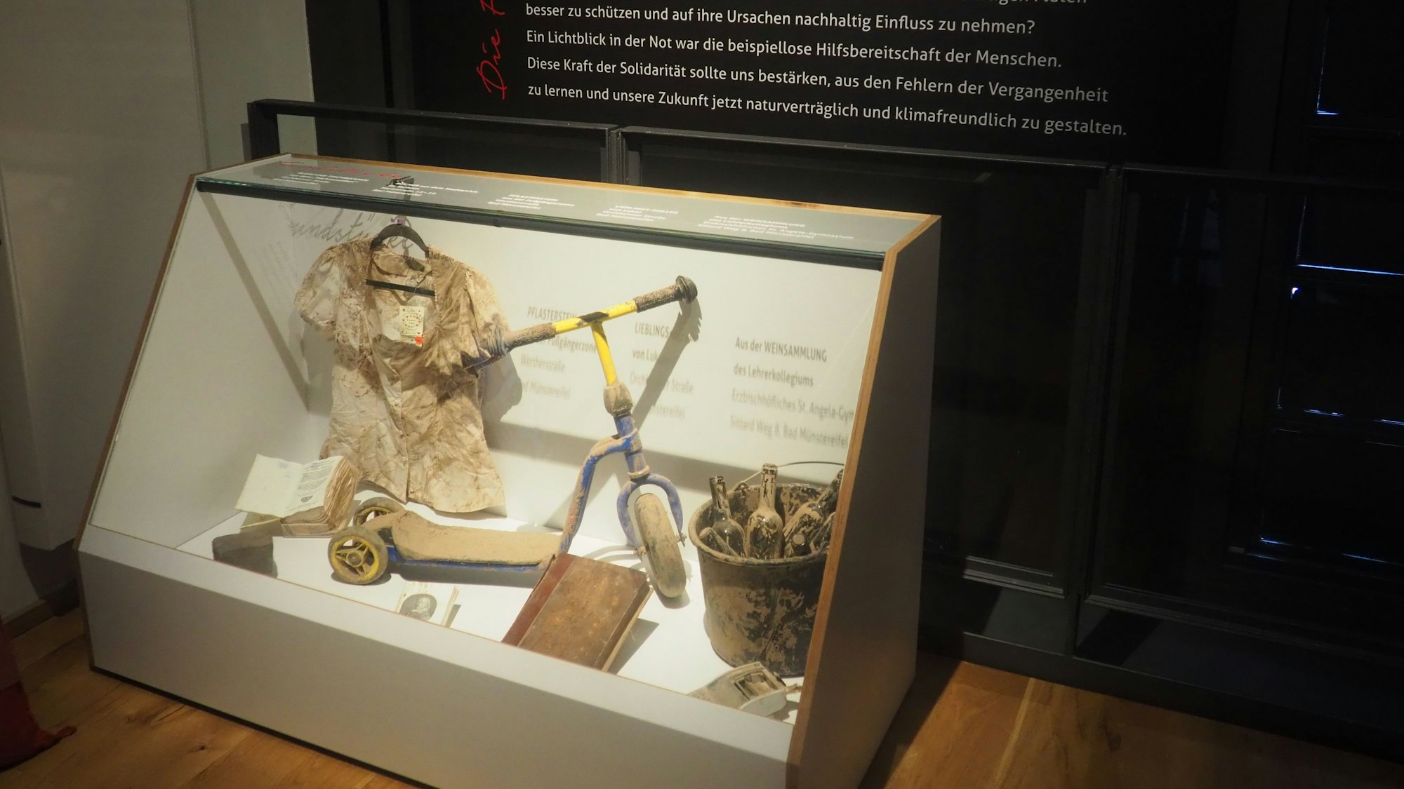 Schlammbedeckte Fundstücke aus dem Flutgebiet sind in einer Vitrine platziert.